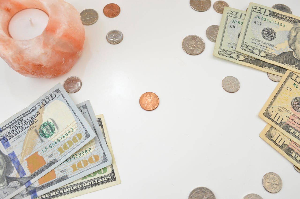 Flat lay image featuring US bills, coins, and a candle on a white background, ideal for financial themes.